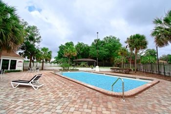 A large swimming pool with a chaise lounge chair and palm trees in the background